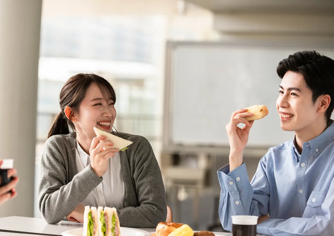 休憩スペースで軽食を取りながら、笑顔で会話を楽しむ同僚二人