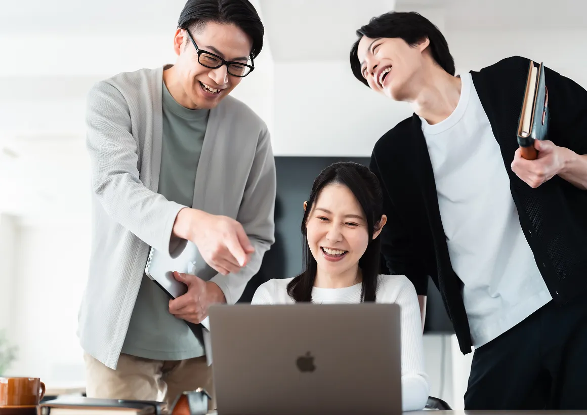 ノートパソコンの画面を囲み、和やかな雰囲気で相談を行うチームメンバー