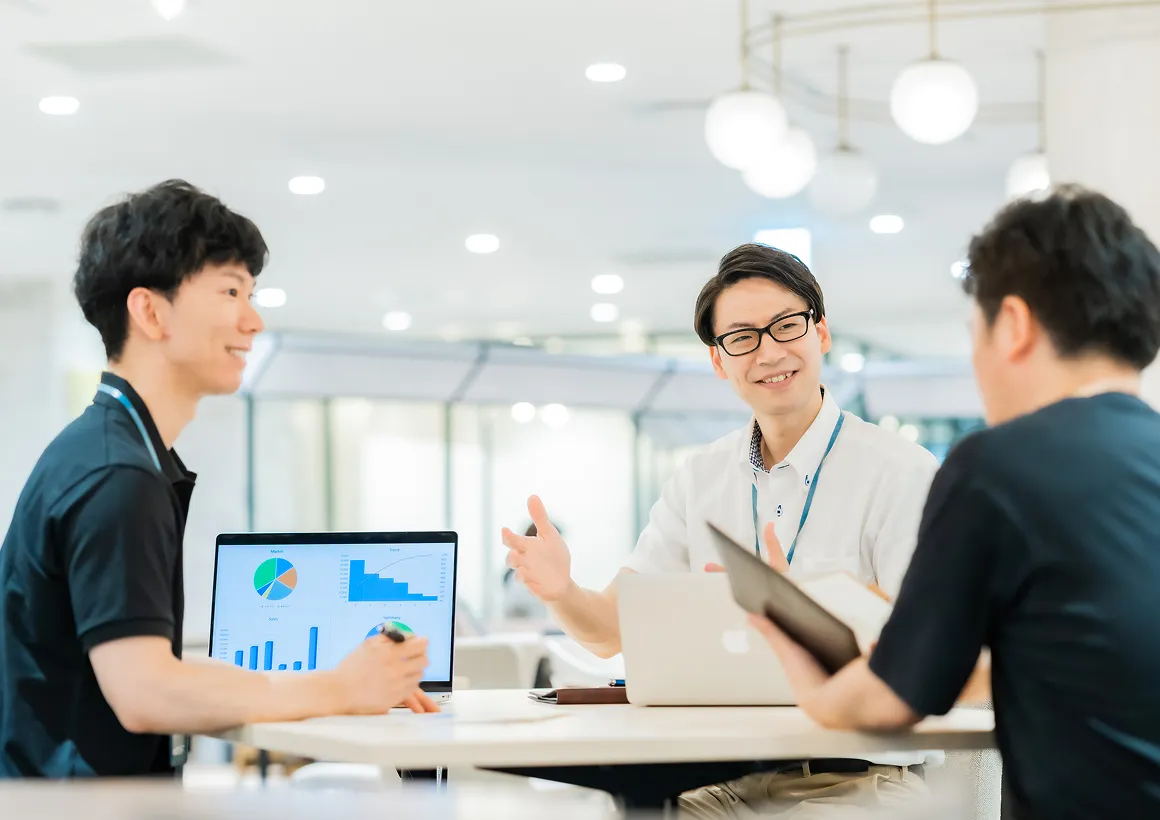 オフィスのテーブルで資料やノートパソコンを使い、データを共有しながら議論するチームのミーティング風景