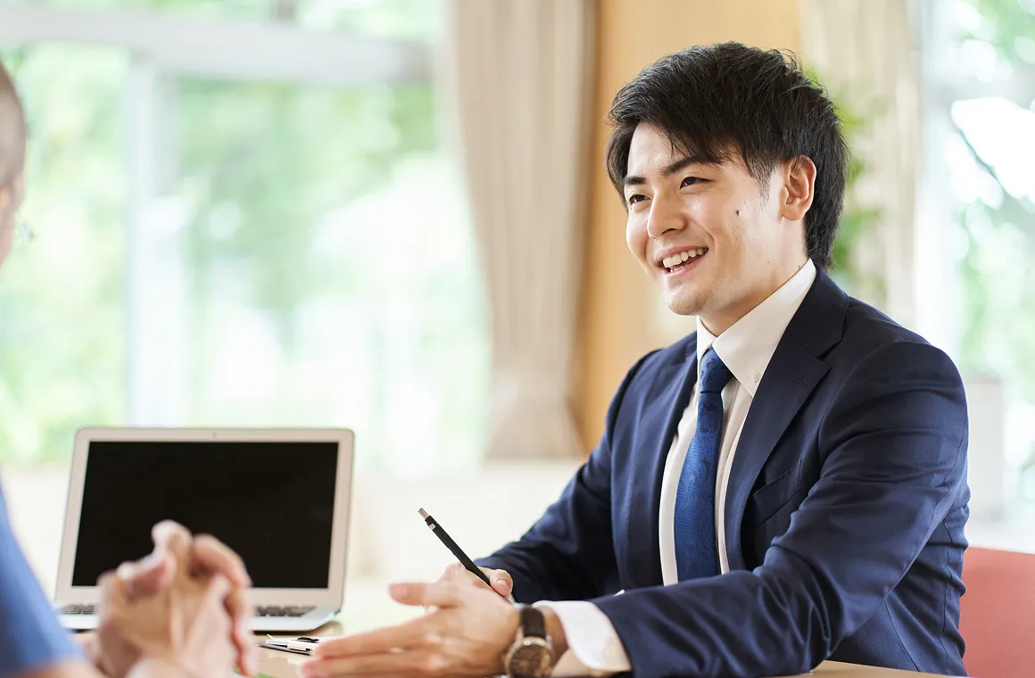 テーブル越しに笑顔で説明を行うスーツ姿の男性と相談中の相手