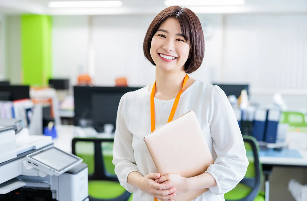 オフィスでノートパソコンを抱え、笑顔で立つスタッフのポートレート