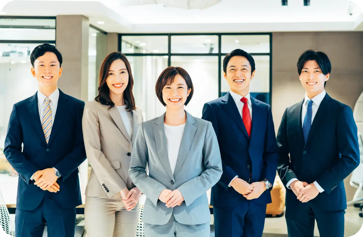 スーツを着たビジネスチームがオフィスで並び、笑顔でカメラに向かって立っている様子